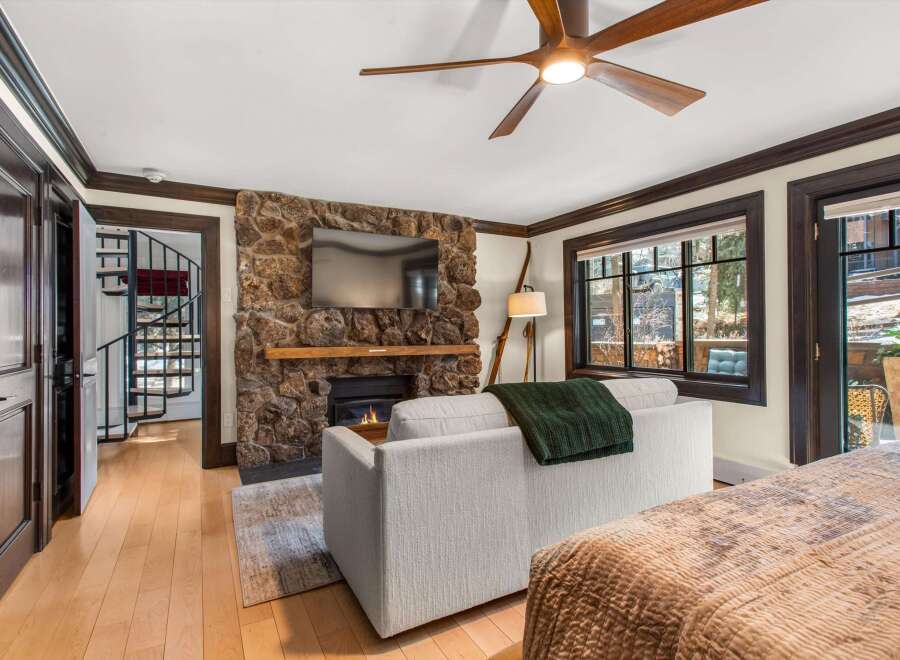 Experience cozy living in this charming room featuring a rustic stone fireplace with a mounted television and a comfortable sofa adorned with a plush green throw.