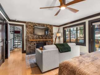 Experience cozy living in this charming room featuring a rustic stone fireplace with a mounted television and a comfortable sofa adorned with a plush green throw.