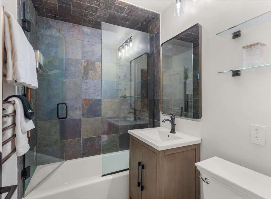 This modern bathroom features a stunning slate tile shower and bathtub surround, complemented by a sleek glass enclosure.