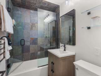 This modern bathroom features a stunning slate tile shower and bathtub surround, complemented by a sleek glass enclosure.