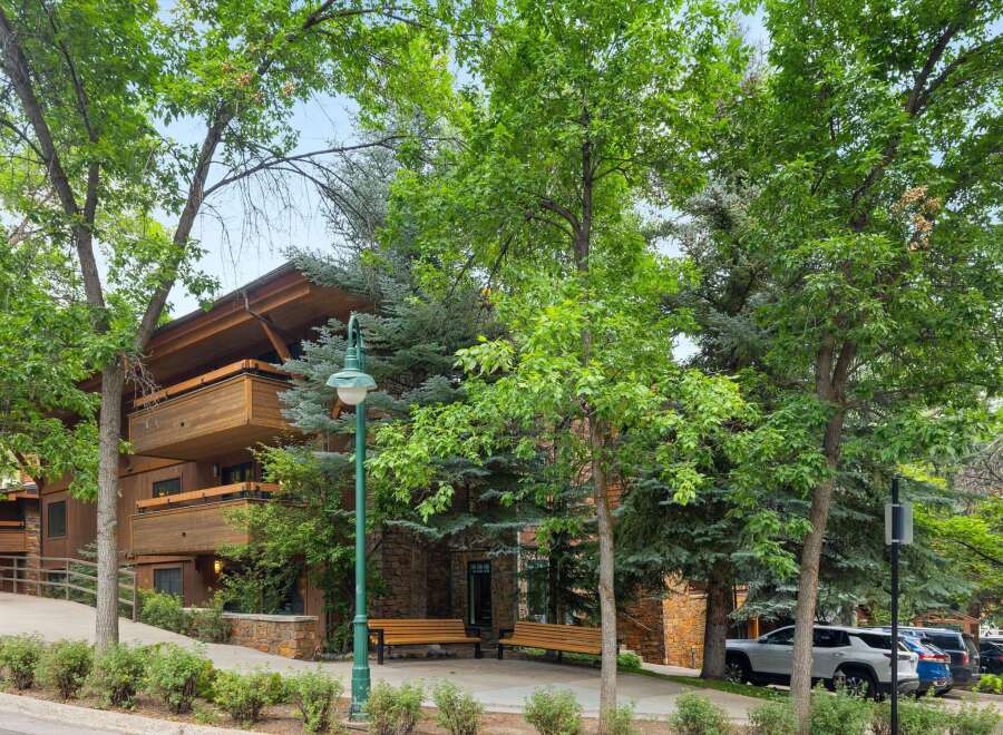 Experience the charm of this multi-story building featuring natural wood siding and stone accents, complemented by ample balconies perfect for enjoying the surrounding greenery.