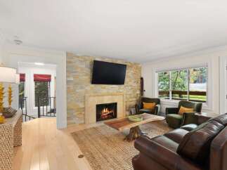 Cozy up by the natural stone fireplace in this inviting living room, featuring plush leather seating and two accent chairs perfect for conversation.