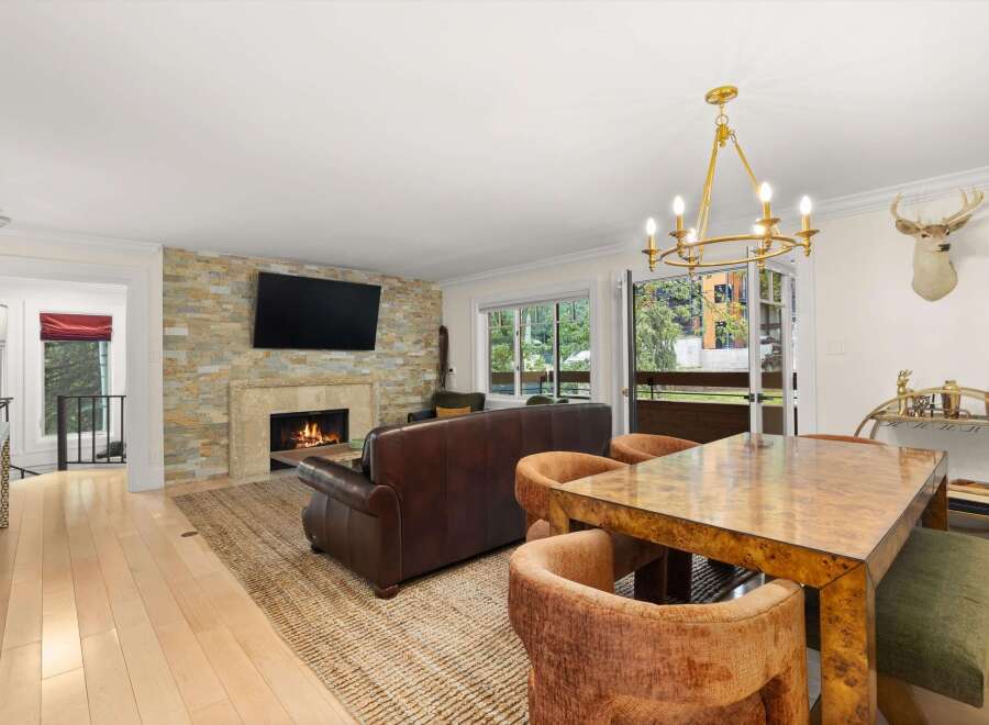 Experience elegant living in this beautifully appointed dining and living area, featuring a cozy fireplace with a stacked stone accent wall and a large flat-screen TV.