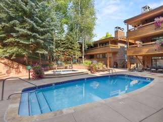 Enjoy a refreshing dip in the sparkling blue pool or relax in the adjacent hot tub, surrounded by lush greenery and mountain-style architecture.
