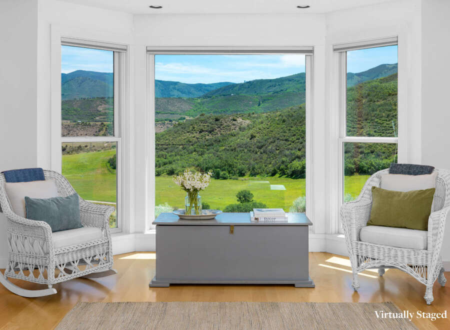 Enjoy breathtaking mountain views from this charming seating area, featuring two wicker rocking chairs and a rustic grey storage chest.