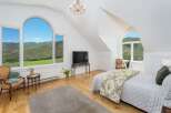 Experience breathtaking mountain views from this stunning bedroom, featuring a grand arched window that floods the space with natural light.