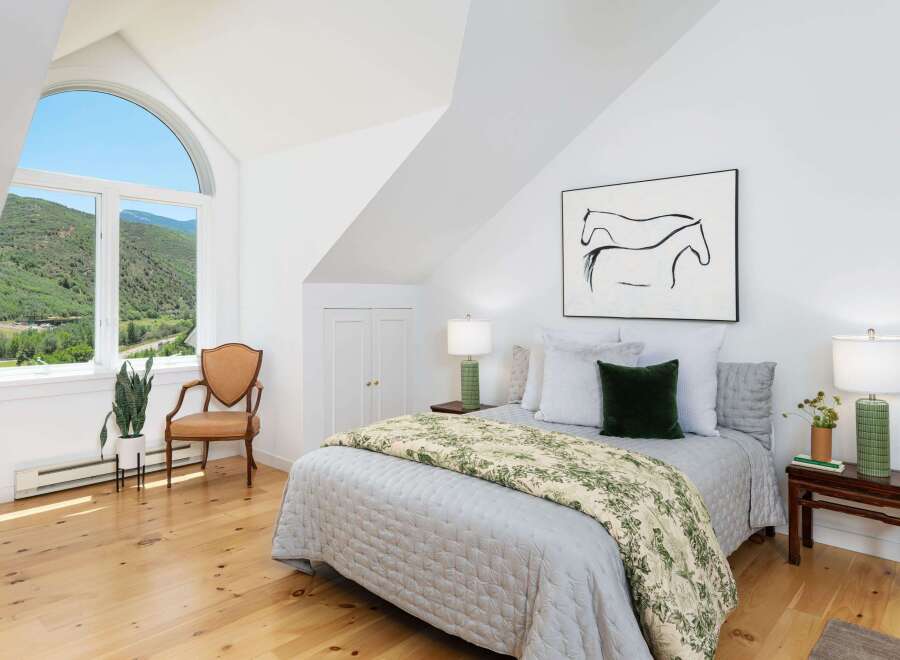 Experience serene mountain living in this charming bedroom, featuring a large arched window with breathtaking views of lush green hills.
