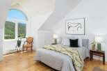Experience serene mountain living in this charming bedroom, featuring a large arched window with breathtaking views of lush green hills.