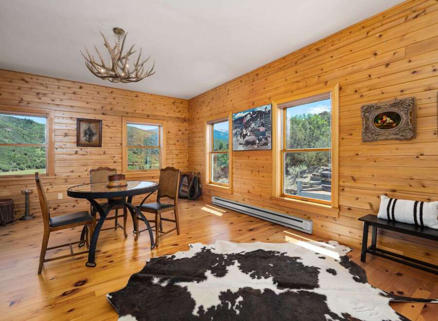 Experience rustic charm in this wood-paneled room, featuring a dining area with a glass-top table and chairs, perfect for intimate meals.