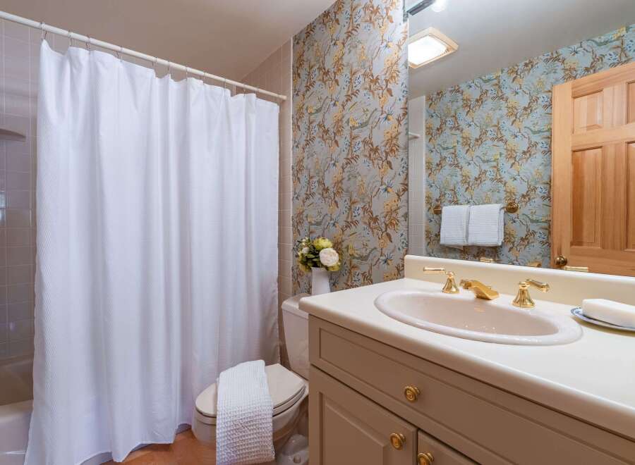 This charming bathroom features a classic floral wallpaper and a white tiled shower with a textured shower curtain.