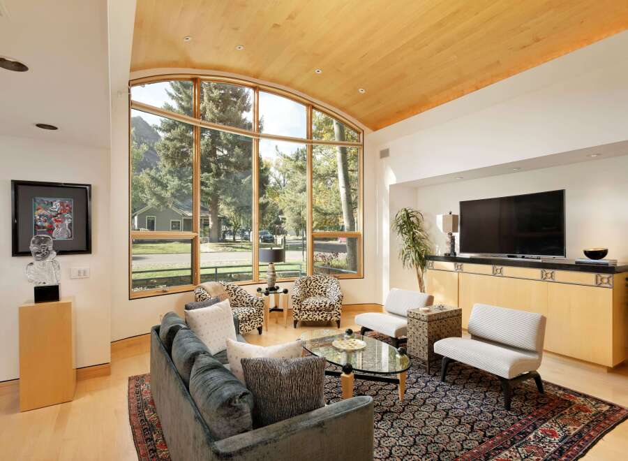 Experience luxurious living in this stunning great room, featuring a soaring vaulted ceiling with natural wood accents and a magnificent arched window framing breathtaking mountain and forest views.