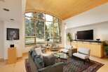 Experience luxurious living in this stunning great room, featuring a soaring vaulted ceiling with natural wood accents and a magnificent arched window framing breathtaking mountain and forest views.