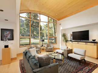 Experience luxurious living in this stunning great room, featuring a soaring vaulted ceiling with natural wood accents and a magnificent arched window framing breathtaking mountain and forest views.