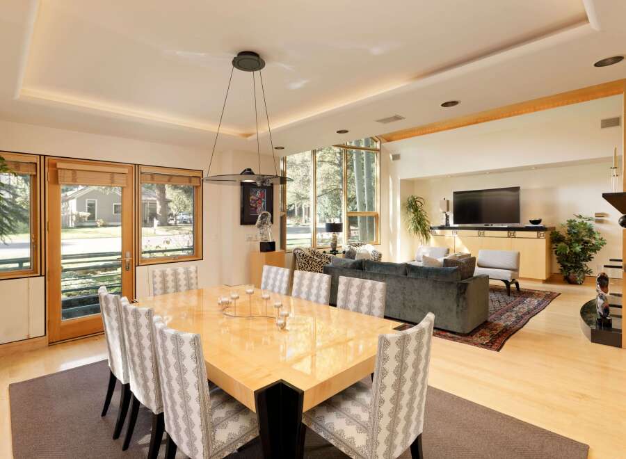 Experience elegant dining and living in this spacious open-concept home, featuring a large, glossy dining table surrounded by upholstered chairs.
