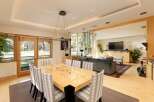 Experience elegant dining and living in this spacious open-concept home, featuring a large, glossy dining table surrounded by upholstered chairs.