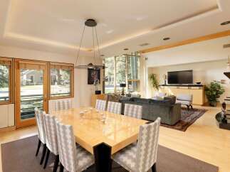 Experience elegant dining and living in this spacious open-concept home, featuring a large, glossy dining table surrounded by upholstered chairs.