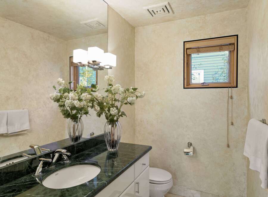 This elegant bathroom features a spacious vanity with a dark green marble countertop and a white undermount sink, complemented by modern chrome fixtures.