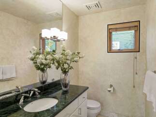This elegant bathroom features a spacious vanity with a dark green marble countertop and a white undermount sink, complemented by modern chrome fixtures.