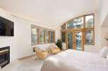 Experience luxury mountain living in this stunning bedroom featuring a cozy fireplace and a large, arched window offering breathtaking views of the surrounding trees and mountains.