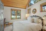 Experience serene living in this charming bedroom, featuring a vaulted wood-paneled ceiling and large windows that flood the space with natural light.