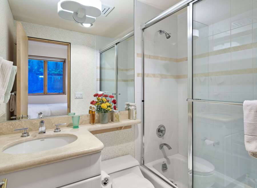 This bright and airy bathroom features a spacious vanity with a stone countertop and a modern sink, complemented by a large mirror reflecting the elegant tiling.