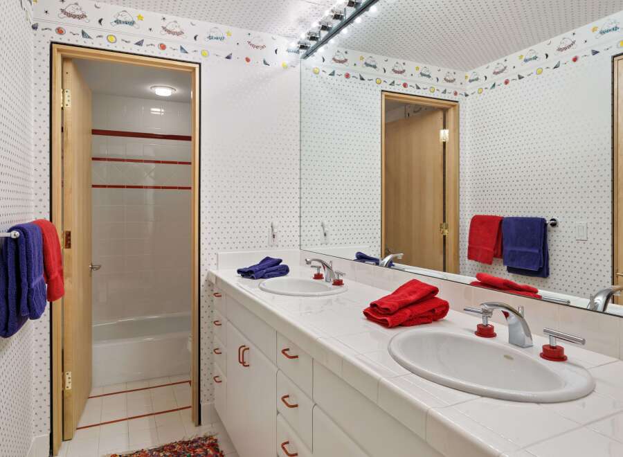 This charming bathroom features a double vanity with white tile countertops and a playful star and moon wallpaper.