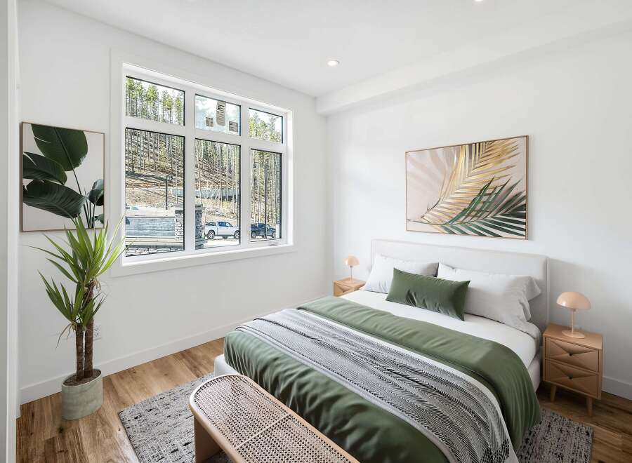 Experience modern comfort in this beautifully staged bedroom, featuring a large window with scenic forest views.