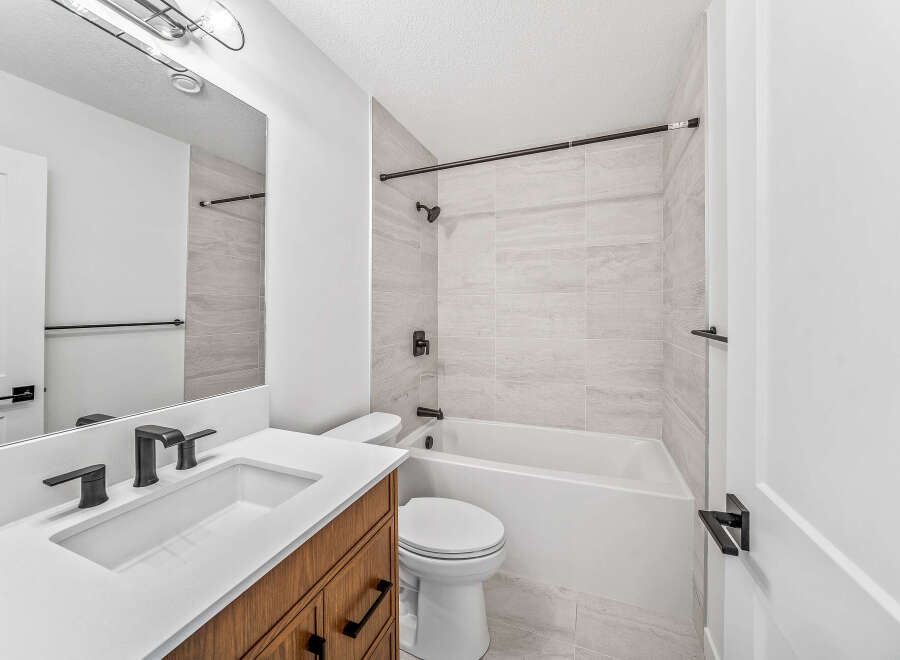This modern bathroom features a sleek vanity with a white countertop and dark wood cabinetry, complemented by black fixtures.
