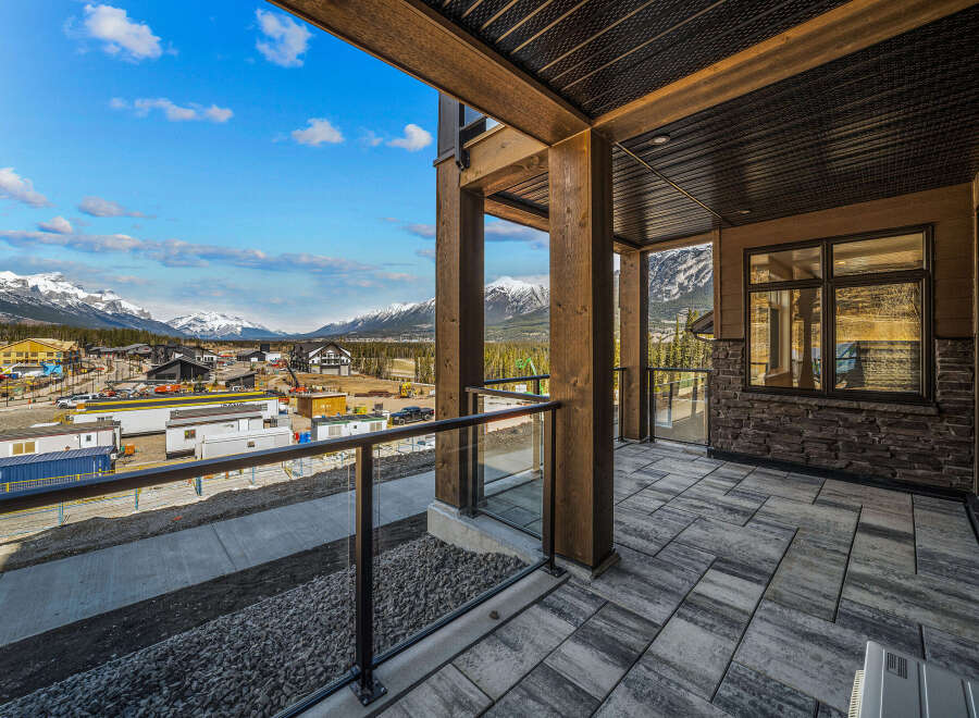 Experience breathtaking mountain views from this stunning property, featuring a spacious balcony with modern glass railings and a covered wooden ceiling.