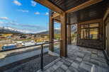 Experience breathtaking mountain views from this stunning property, featuring a spacious balcony with modern glass railings and a covered wooden ceiling.
