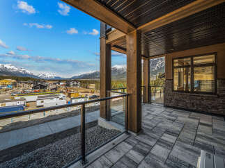 Experience breathtaking mountain views from this stunning property, featuring a spacious balcony with modern glass railings and a covered wooden ceiling.