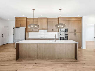 Experience modern living in this stunning kitchen featuring sleek, light wood cabinetry and a spacious island with a waterfall countertop.