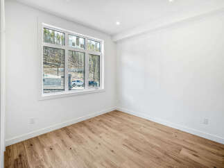 Discover modern living in this bright and airy room featuring a large window with scenic views of a wooded hillside.