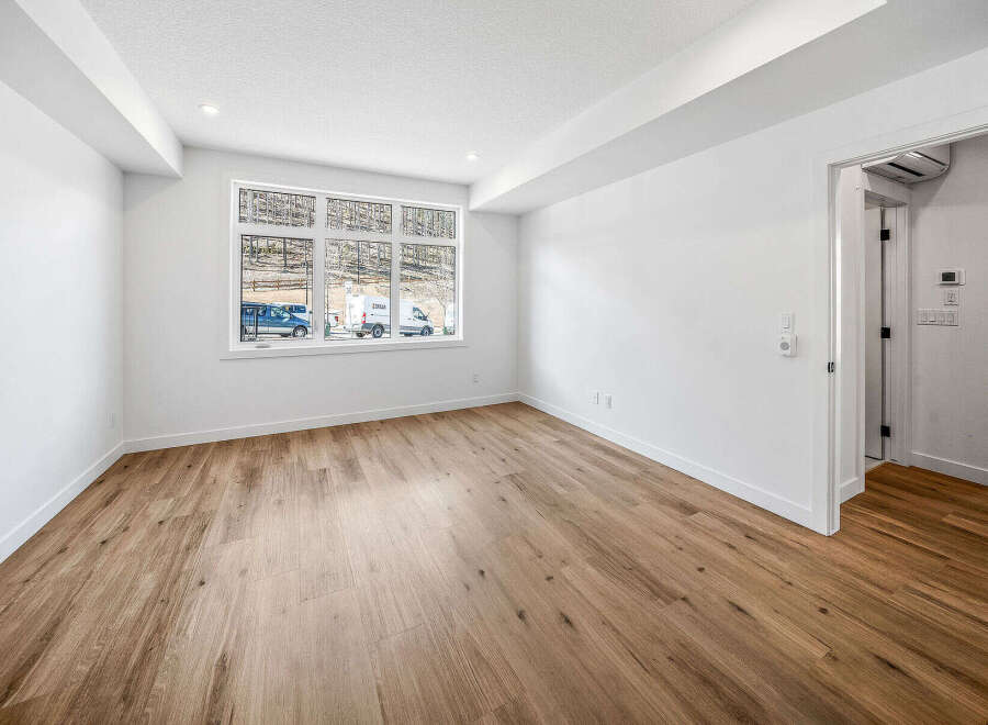 Experience modern living in this bright and airy room featuring a large window with scenic views and elegant hardwood flooring.