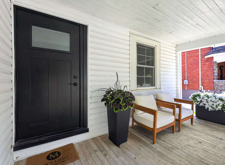 Step onto the charming porch of this inviting home, featuring a sleek black front door and a welcoming doormat.