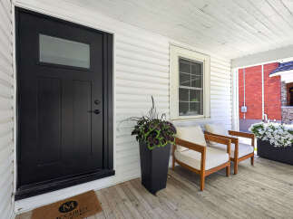 Step onto the charming porch of this inviting home, featuring a sleek black front door and a welcoming doormat.