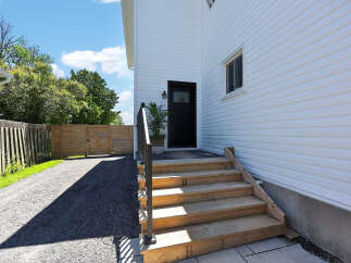 Discover this charming home featuring a welcoming entrance with a black door and a stylish black railing leading up a wooden staircase.