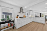 This modern white kitchen features sleek white cabinetry, a stainless steel range hood, and a gas stovetop.