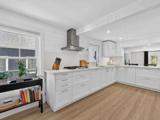 This modern white kitchen features sleek white cabinetry, a stainless steel range hood, and a gas stovetop.