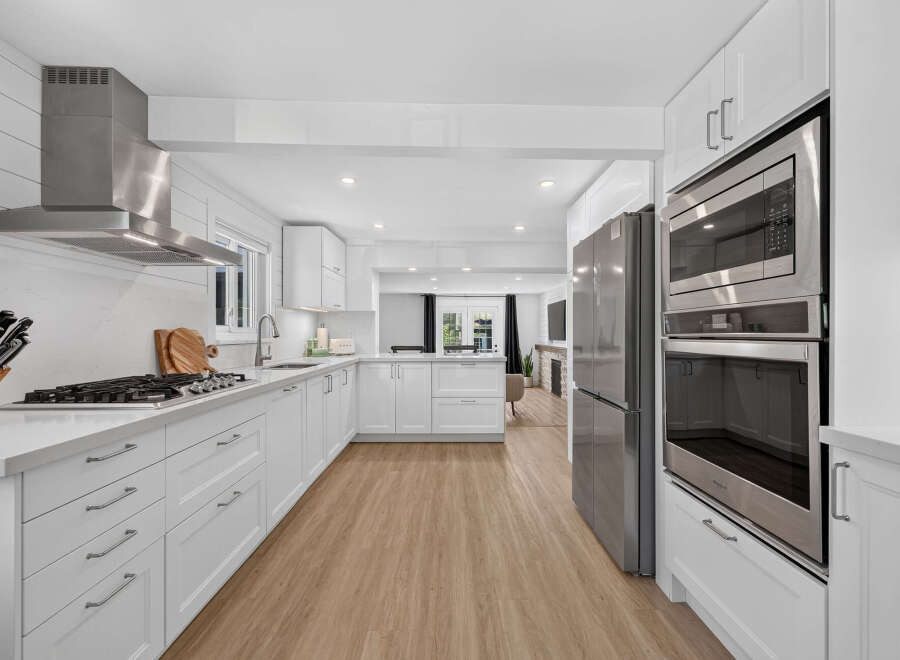 Experience modern living in this stunning white kitchen, featuring sleek stainless steel appliances, including a gas range and double ovens.
