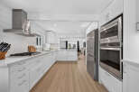 Experience modern living in this stunning white kitchen, featuring sleek stainless steel appliances, including a gas range and double ovens.