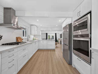 Experience modern living in this stunning white kitchen, featuring sleek stainless steel appliances, including a gas range and double ovens.