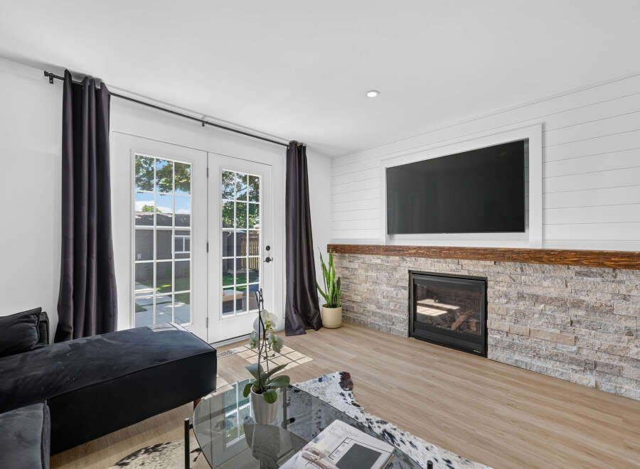 Experience modern living in this beautifully appointed living room, featuring a sleek fireplace with a stacked stone surround and a rustic wood mantel.