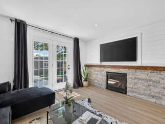 Experience modern living in this beautifully appointed living room, featuring a sleek fireplace with a stacked stone surround and a rustic wood mantel.