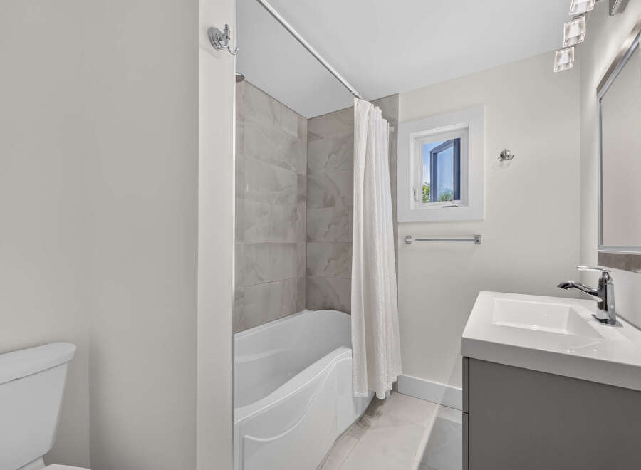 This modern bathroom features a sleek white bathtub with elegant marble-patterned tiles and a convenient white shower curtain.
