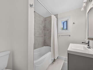 This modern bathroom features a sleek white bathtub with elegant marble-patterned tiles and a convenient white shower curtain.