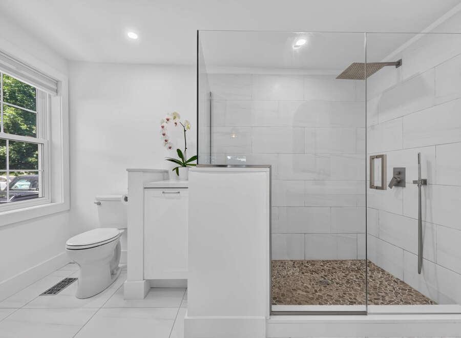 Experience modern luxury in this pristine white bathroom, featuring a sleek glass-enclosed shower with a pebble tile floor and a rainfall showerhead.
