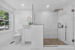 Experience modern luxury in this pristine white bathroom, featuring a sleek glass-enclosed shower with a pebble tile floor and a rainfall showerhead.
