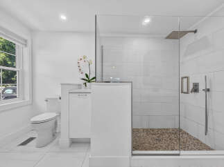 Experience modern luxury in this pristine white bathroom, featuring a sleek glass-enclosed shower with a pebble tile floor and a rainfall showerhead.