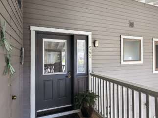 Welcome to this charming property featuring a dark gray front door with a glass pane and a decorative dragonfly accent on the exterior wall.